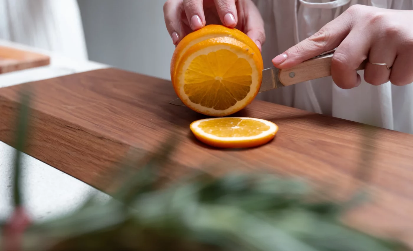 Vrouw snijdt plakjes van een sinaasappel, met rozemarijn